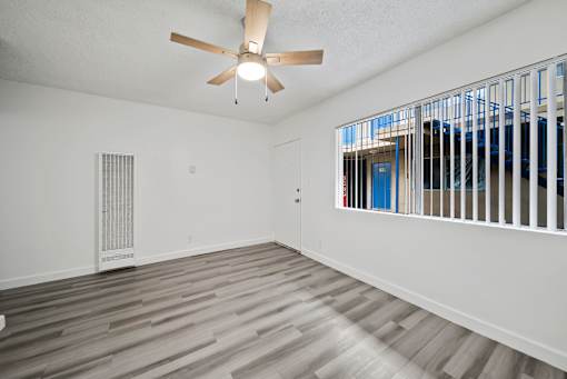 A room with a ceiling fan and a window with bars.