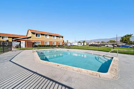 A small pool in a concrete area with a building in the background.