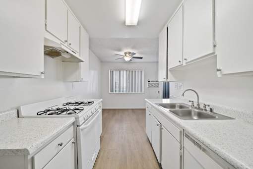 A white kitchen with a stove, sink, and cabinets.