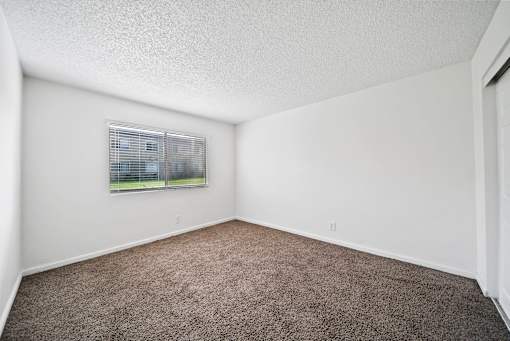 A room with a carpeted floor and a window with blinds.