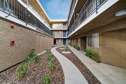 A concrete pathway leads through a landscaped courtyard between two apartment buildings.