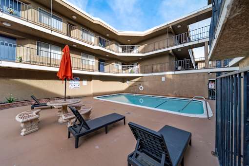 A pool area with a red umbrella and black lounge chairs.
