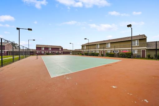 A tennis court with a red surface and a green surface in the middle.