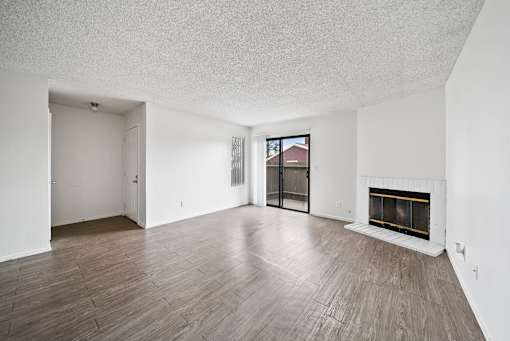 A large empty room with a fireplace and wood flooring.