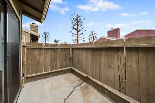A concrete patio with a wooden fence and a tree in the background.