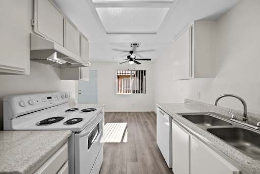 A white kitchen with a stove, sink, and a fan.