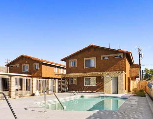 A house with a brown exterior and a pool in front.