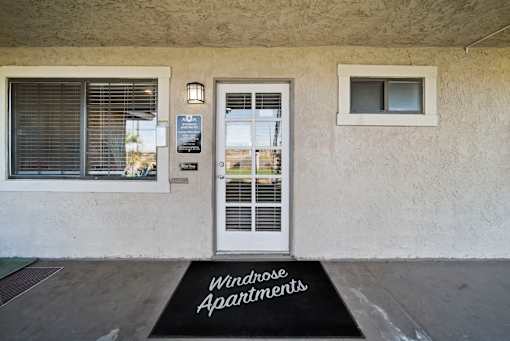 The entrance to a building with a sign that says "Windrose Apartments" on the doormat.
