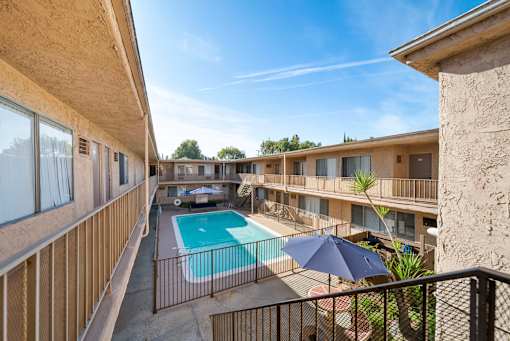 A balcony overlooks a pool and a patio with chairs and an umbrella.