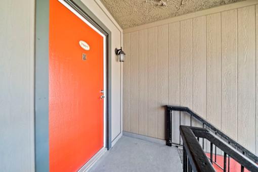 A bright orange door with a silver handle and a small round plate above it.