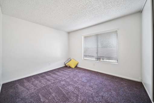 A room with a window and a yellow bag on the floor.
