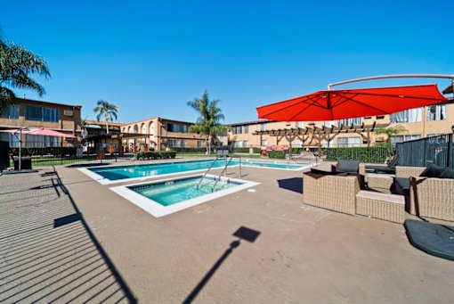 A pool with a red umbrella and a building in the background.