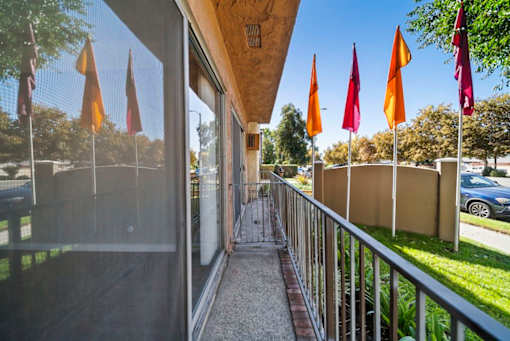 A balcony with a metal railing and a glass door leading to a patio with orange flags.
