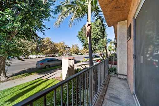 A balcony with a metal railing and a view of a street with a car and trees.