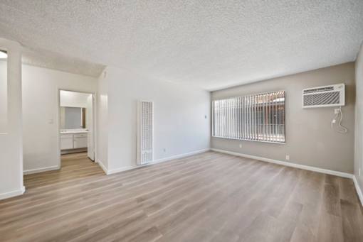 A spacious room with wooden flooring and a window with blinds.