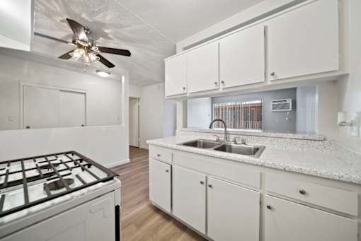 A kitchen with a white stove top oven and white cabinets.