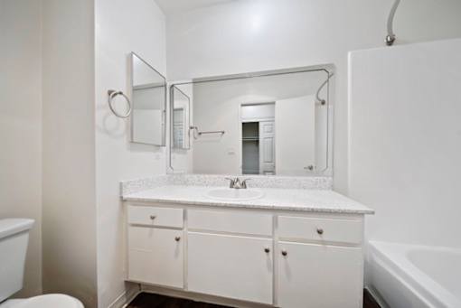 A white bathroom with a sink, mirror, and bathtub.