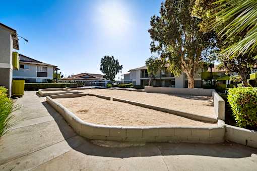 A sandbox in the middle of a concrete area with houses and trees in the background.