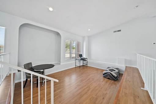 A room with a wooden floor and white walls has a table and chairs in it.