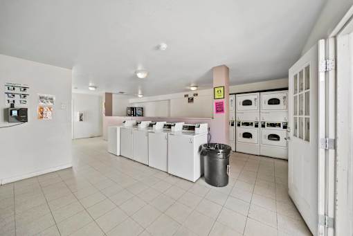 A kitchen with white appliances and a trash can.