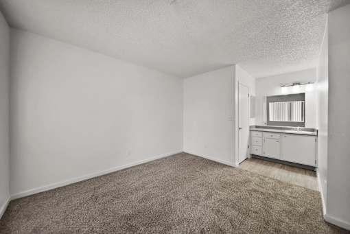 A room with a carpeted floor and a small kitchenette in the corner.