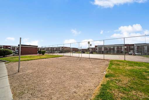 A fenced-in area with a dirt ground and a building in the background.