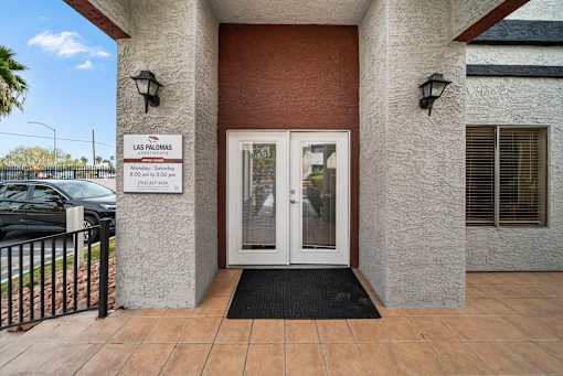 The entrance to a building with a sign that reads "Las Palomas" and a black doormat in front.
