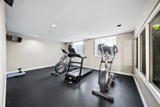 A room with a black floor and white walls has a row of exercise equipment.