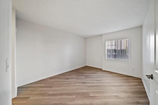 A room with wooden flooring and a window with blinds.