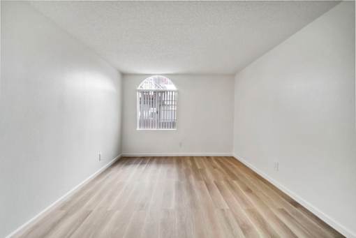 A room with a wooden floor and a window with bars on it.