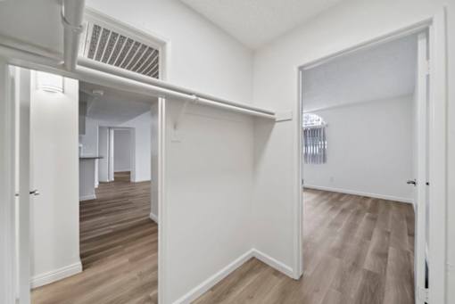 A room with white walls and wooden flooring with a doorway leading to another room.
