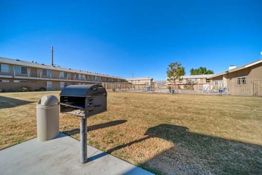 A mailbox sits on a concrete slab in front of a grassy area with apartment buildings in the background.