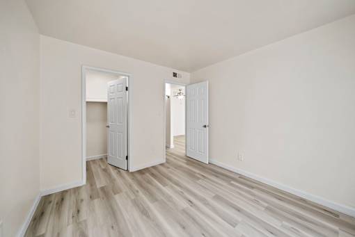 A room with white walls and wood flooring with two doors open.