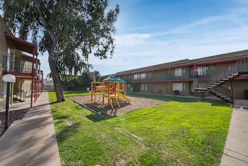 A playground with a slide and swings is surrounded by grass and trees.