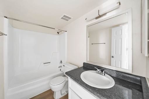 A white bathroom with a black countertop and a white toilet.