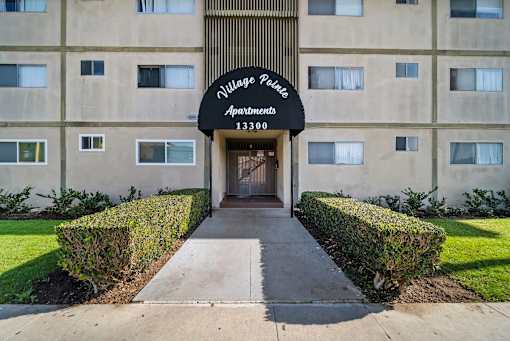 The front of a building with a sign that says "Village Police Apartments 13300".