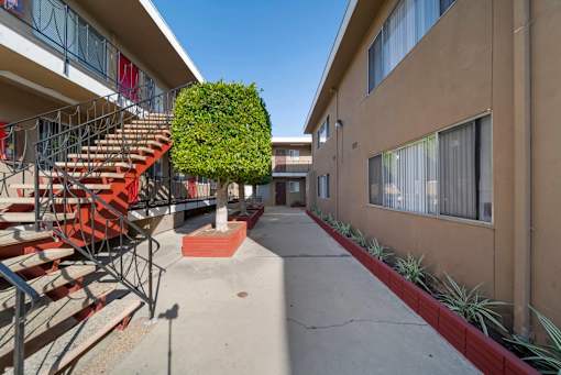 A red staircase with a metal railing is on the left side of a concrete walkway.