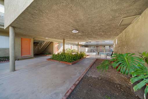 A concrete building with a red door and plants on the side.