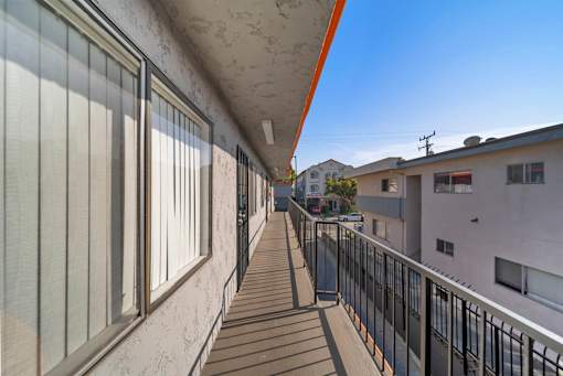 A long balcony with a black railing and a white wall.