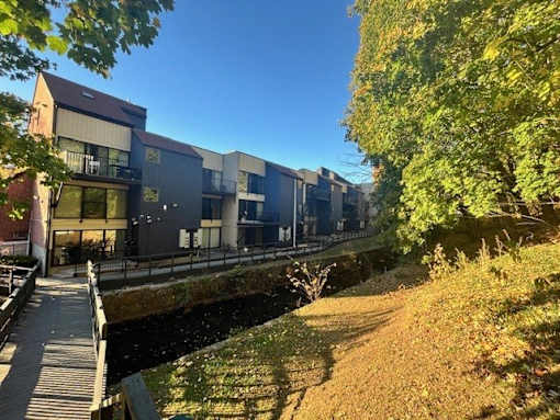 A row of modern buildings line a canal with a wooden walkway alongside.
