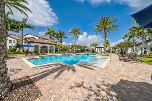 A swimming pool surrounded by palm trees and a brick patio at The Atlantic at Tradition, Port St Lucie