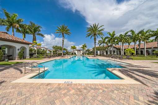 A swimming pool surrounded by palm trees and a brick patio at The Atlantic at Tradition, Port St Lucie
