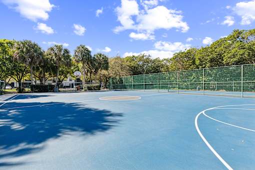 A blue tennis court surrounded by a green fence and trees at The Atlantic Preserve, Plantation, FL 33322
