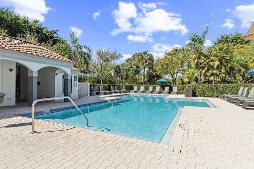 A swimming pool surrounded by a tiled patio and a white building with a red roof at The Atlantic Preserve, Plantation, FL