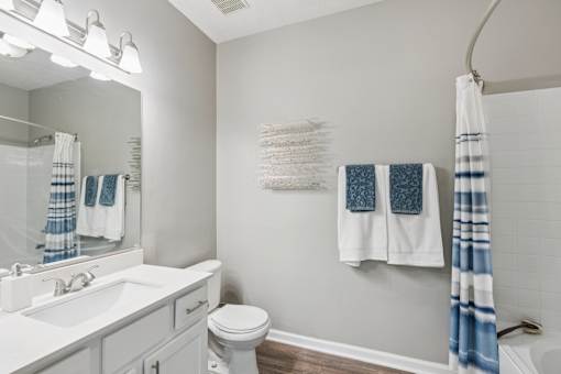 A white bathroom with a white toilet, sink, and a blue and white towel hanging on the wall at The Atlantic Canton Ridge, Georgia