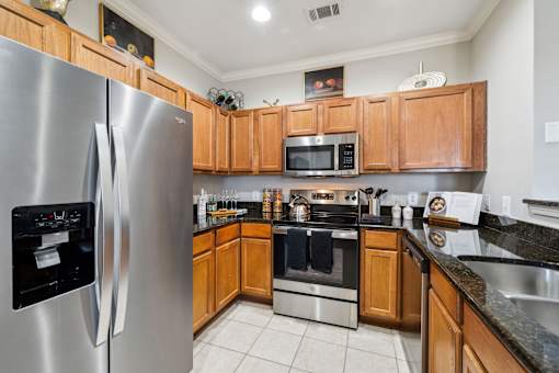 A modern kitchen with wooden cabinets and stainless steel appliances at The Atlantic Stone Oak Apartments, San Antonio