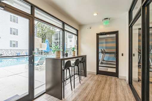 A patio with a bar and chairs is shown with a view of a pool and buildings outside at The Atlantic Loring Heights, Atlanta, Georgia
