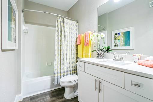 A bathroom with a white toilet, a white sink, and a shower with a yellow and white curtain at The Atlantic Buckhead Apartments, Atlanta, 30305