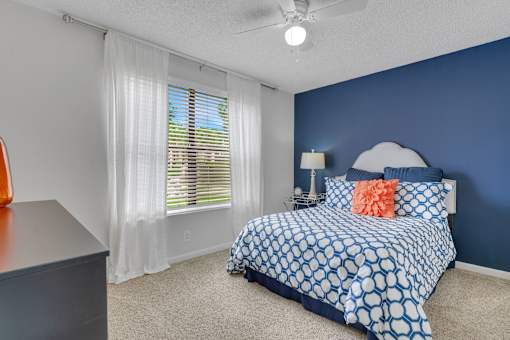 A bedroom with a bed, nightstand, and window with blinds at Boca Colony Apartments, Boca Raton, FL, 33433
