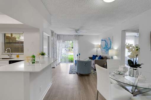 A modern living room with a glass table and white chairs at Boca Colony Apartments, Florida